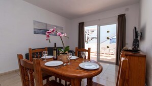 Un coin repas avec une table en bois dressée pour quatre personnes, un vase rempli de fleurs roses et une vue sur le balcon extérieur.