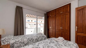 A bedroom with two beds, wooden wardrobe, and a window with curtains. - Las Blanquitas 9 (Playa de Las Americas)