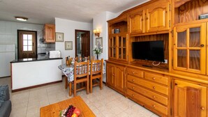 A kitchen with wooden cabinets, a dining table with chairs, and a television on a wooden cabinet. - Las Blanquitas 9 (Playa de Las Americas)