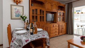 A dining area with a table set for four, wooden cabinets, a television, and a window with a view of the outside. - Las Blanquitas 9 (Playa de Las Americas)
