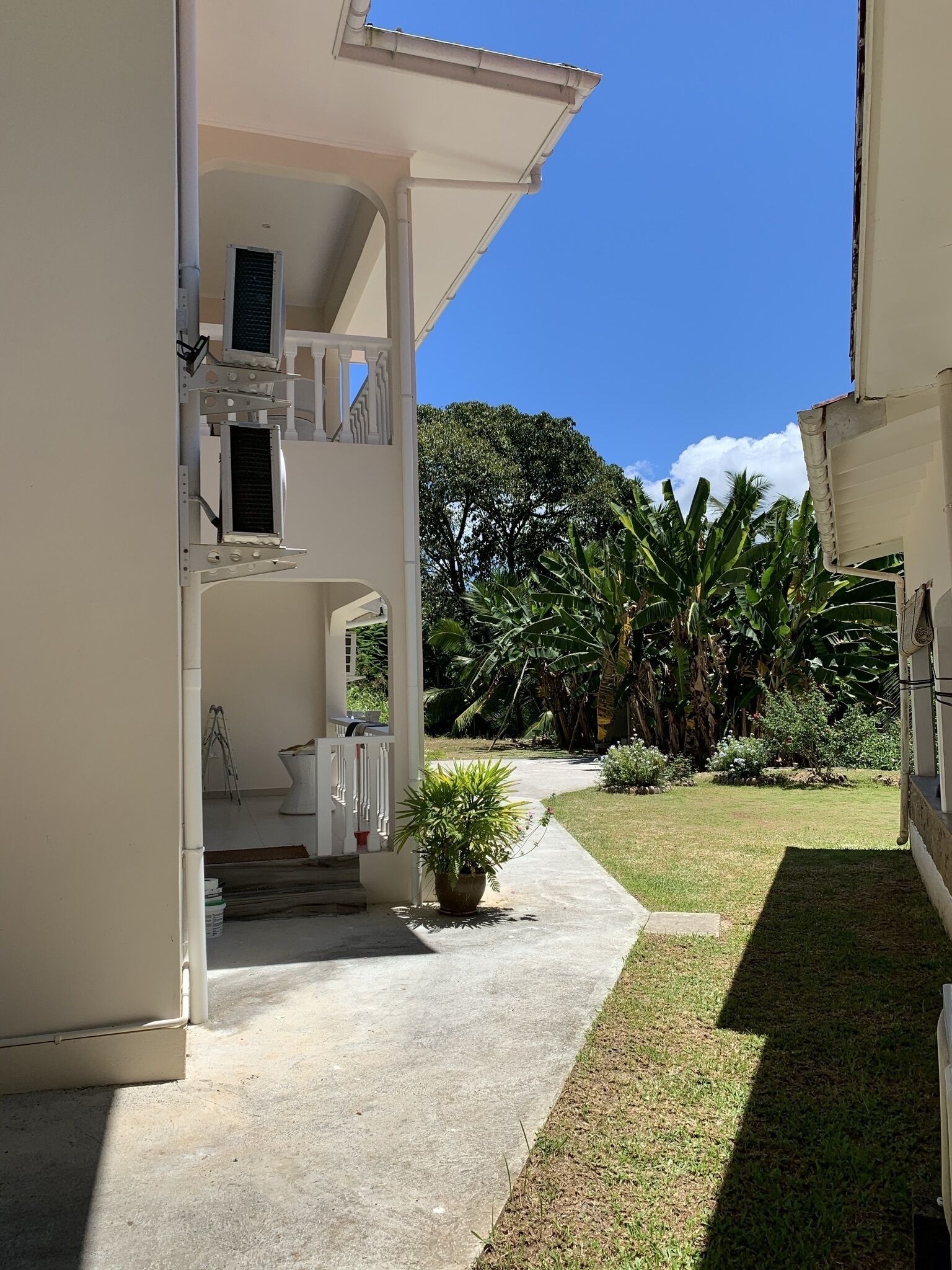 A two-story building with a covered porch and a small garden area with potted plants and a lawn.