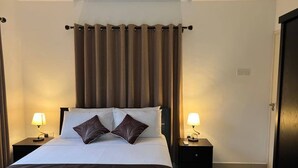 A neatly made bed with white and brown bedding, two bedside lamps, and a curtain. - Paul's Residence (Mahé Island)