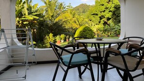 A room with a view of a lush garden, a round table with chairs, and a metal drying rack. - Paul's Residence (Mahé Island)