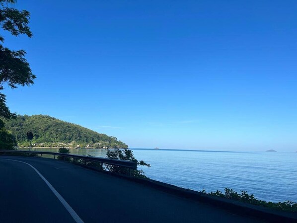 A coastal road with a clear view of the sea and a hilly landscape.