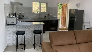 A modern kitchen with a central island, two bar stools, a sofa, and a refrigerator. - Paul's Residence (Mahé Island)
