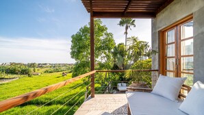 A balcony with a bed, a view of a green field, and a wooden railing.