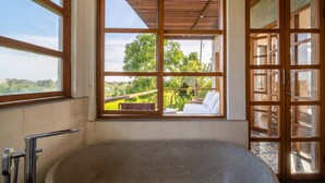 A modern bathroom with a freestanding bathtub, large windows, and a view of a garden.