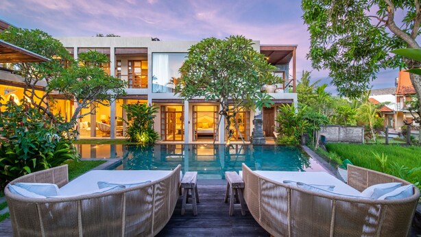 A modern house with a swimming pool, wicker furniture, and lush greenery.