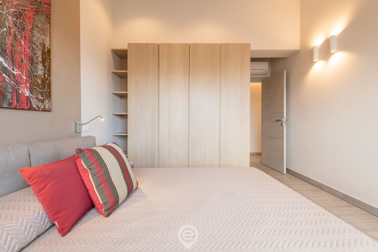A modern bedroom with a large bed, a wardrobe, and a painting on the wall.