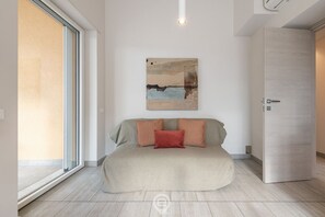 A modern bedroom with a large bed, a sliding glass door to a balcony, and a wooden wardrobe.
