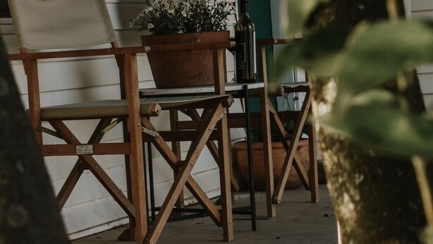 Een houten stoel met kussen en een bloempot op een veranda.