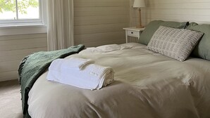 Een slaapkamer met een groot bed, een schilderij aan de muur, een raam met gordijnen en een nachtkastje met een lamp.