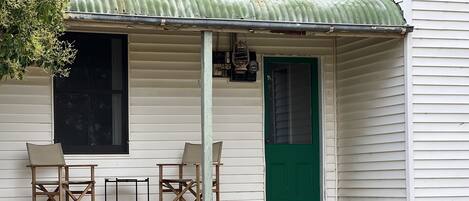 A porch with two wooden chairs, a green door, and potted plants.