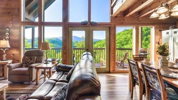 L’intérieur chaleureux d’un chalet avec un canapé en cuir, des meubles en bois et de grandes fenêtres offrant une vue sur les montagnes.