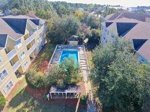 A residential building with a swimming pool surrounded by trees and a small garden area.