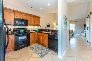Una cocina con armarios de madera, microondas negro, estufa y lavavajillas.