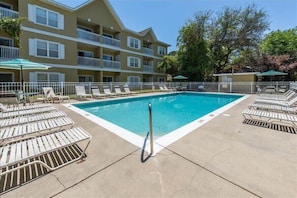 A swimming pool with lounge chairs and umbrellas, surrounded by a white fence, with a multi-story building in the background. - 2 Adult Bikes! Walk to Pool & Beach! Heart of Seagrove - Summer Breeze at Seagrove Beach 30A (Santa Rosa Beach)
