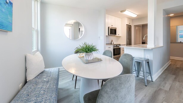 A modern living room with a round dining table, grey chairs, a bench, and a large mirror on the wall. - Prime Eastport Location - Waterfront Condo w Pool & Parking (Annapolis)