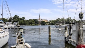 A marina with boats docked, a church in the background, and a calm water body. - Prime Eastport Location - Waterfront Condo w Pool & Parking (Annapolis)