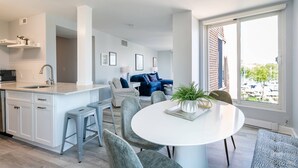A modern kitchen with a central island, a dining area with a round table, and a living room with a blue sofa. - Prime Eastport Location - Waterfront Condo w Pool & Parking (Annapolis)