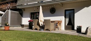 A covered outdoor seating area with wicker furniture, a clock, and potted plants.