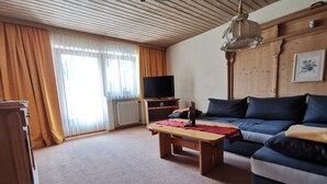 Een woonkamer met een houten plafond, een bank, een salontafel, een televisie en een radiator.