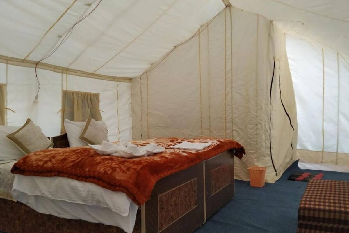 Eine Zelthütte mit einem Bett, Kissen, einer Decke und einem kleinen Tisch.