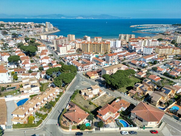 An aerial view of a coastal residential area with a mix of single and multi-story buildings, roads, and a marina. - VELA: House with swimming pool in l'Escala, a few meters from the beach of Riells (L'Escala)