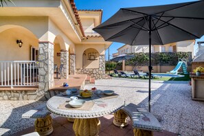A patio area with a round table, outdoor seating, and a pool with a slide. - VELA: House with swimming pool in l'Escala, a few meters from the beach of Riells (L'Escala)