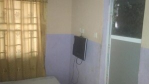 Una habitación con cama, ventana con persianas y un enchufe en la pared.