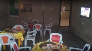 Una habitación con sillas y mesas de plástico, algunas con manteles amarillos. Hay carteles en las paredes y un televisor en la pared.
