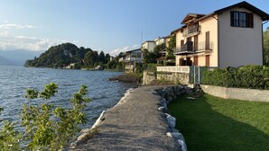 A waterfront property with a stone pathway leading to a grassy area, overlooking a lake with mountains in the background. - Vacation apartment directly on the lake (Leggiuno)