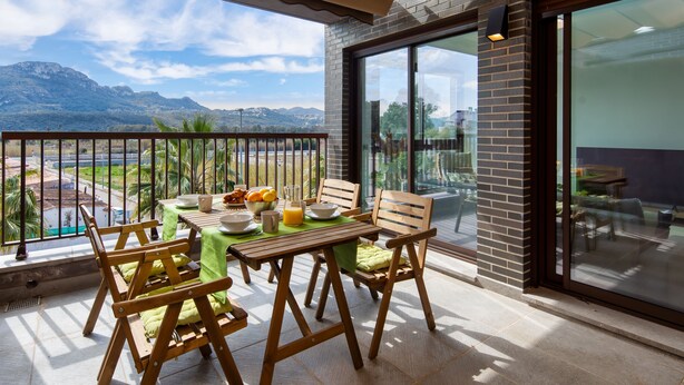 Ein Balkon mit Holztisch, gedeckt für das Frühstück, mit Blick auf eine Berglandschaft.