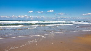Ein Strand mit Wellen, blauem Himmel und vereinzelten Wolken.