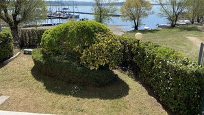 Een verzorgde tuin met verschillende struiken en een kleine boom, een helder uitzicht op een jachthaven met boten, en een rustig meer op de achtergrond.