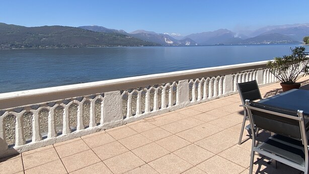 Een terras met uitzicht op een meer en bergen, met een tafel en stoelen.