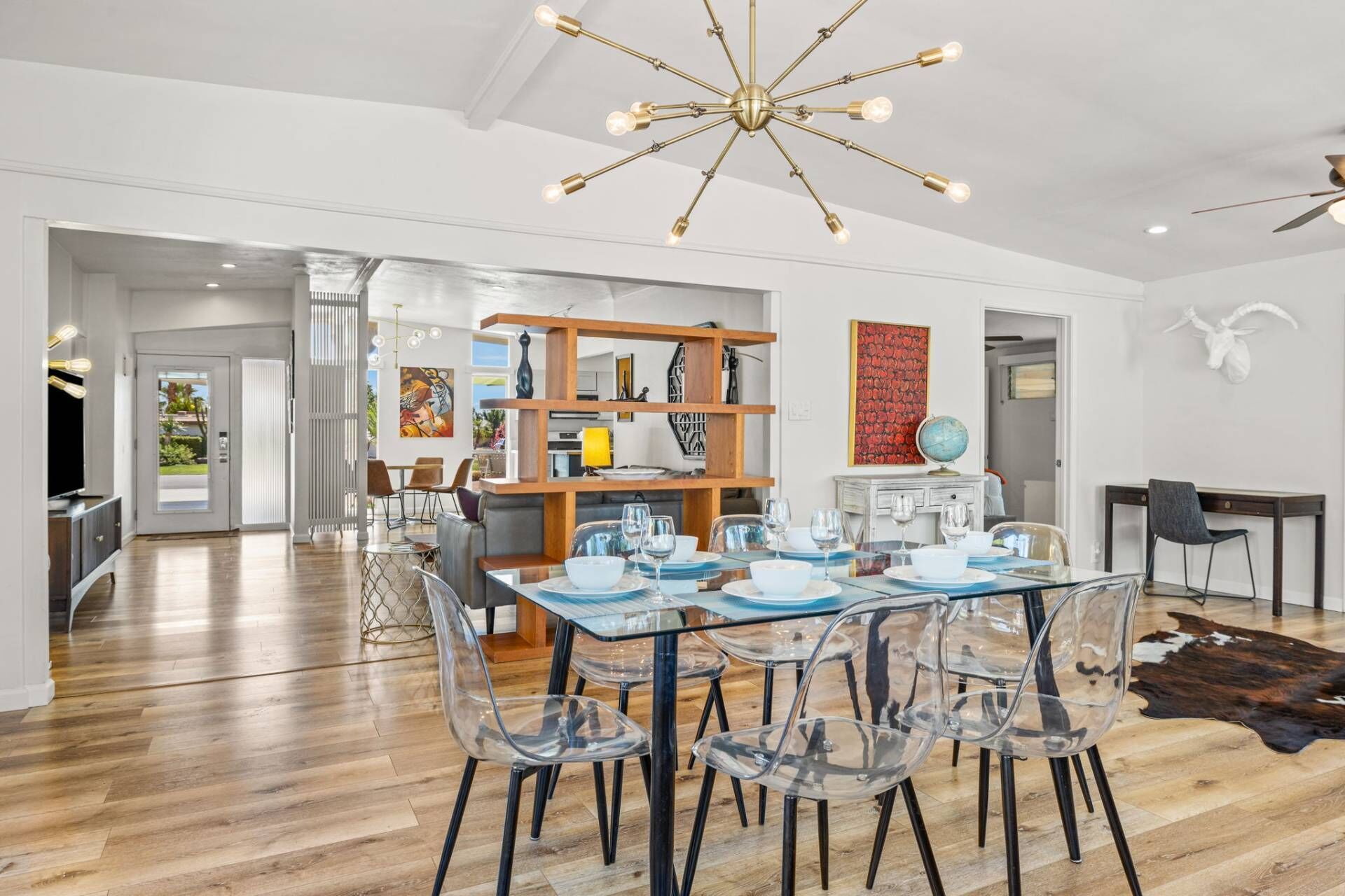 A spacious dining area with a glass table and clear chairs, a wooden bookshelf, and a modern chandelier.
