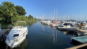 Ein Yachthafen mit vertäuten Booten entlang einer ruhigen Wasserstraße, umgeben von Grünflächen und Bäumen.
