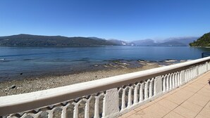 Ein klarer Blick auf einen See mit Bergen im Hintergrund, ein gepflasterter Weg und eine Geländer.