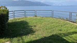 Eine bewachsene Fläche mit einem Metallgeländer, das auf einen See und ferne Berge blickt.