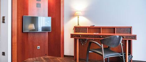 Habitación de hotel con un escritorio de madera, una silla, un televisor montado en la pared y una lámpara sobre el escritorio.