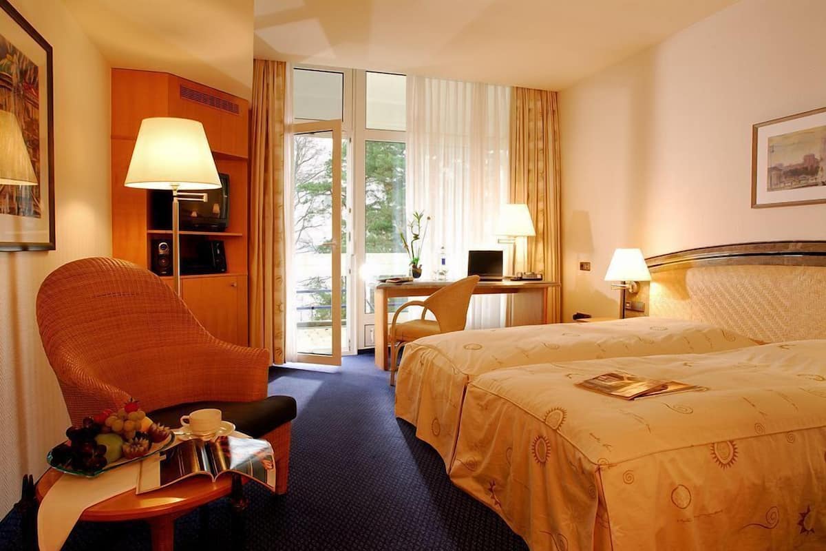 A hotel room with a bed, a desk, a chair, a television, and a lamp.