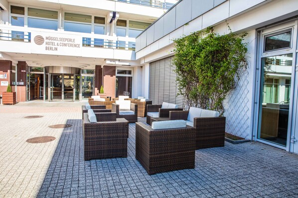 A hotel entrance with outdoor seating and a sign for Mögelseeperle Hotel & Conference Berlin.