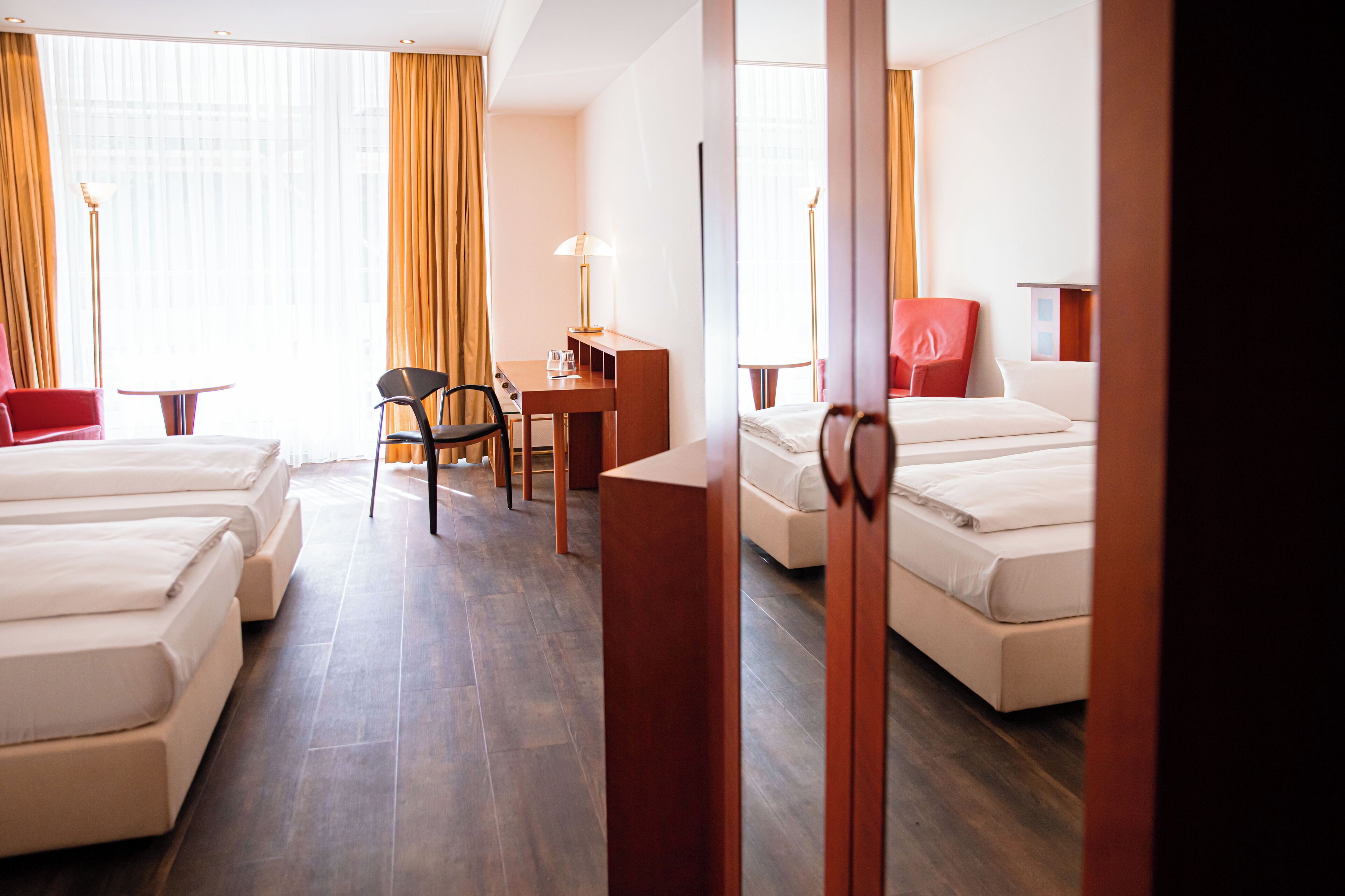 Une chambre d’hôtel avec trois lits, un bureau, une chaise et une lampe.
