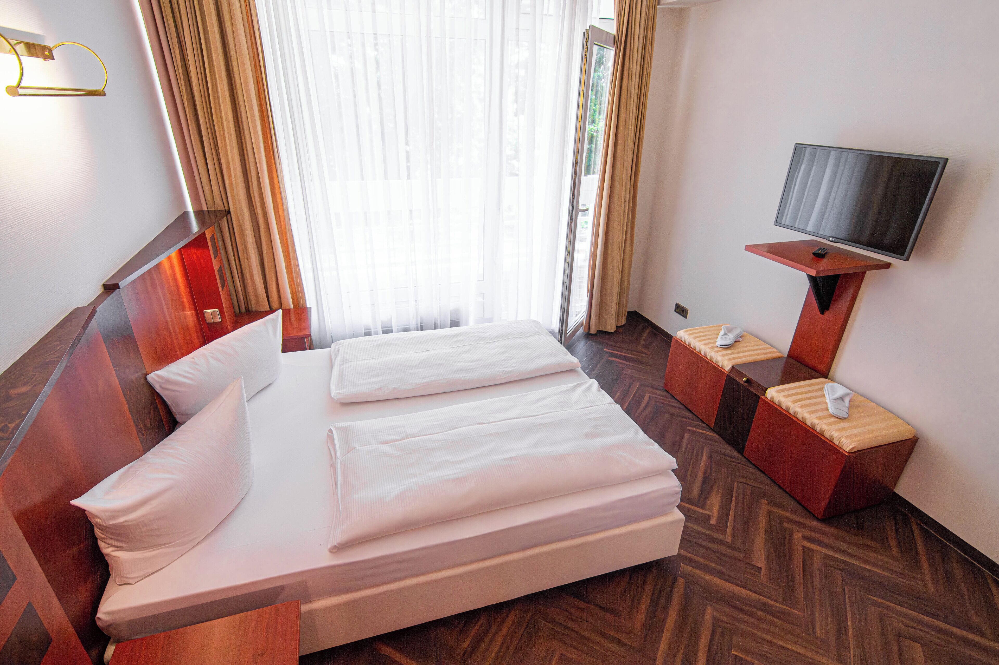 Ein Hotelzimmer mit Bett, Fernseher und einem Fenster mit Vorhängen.