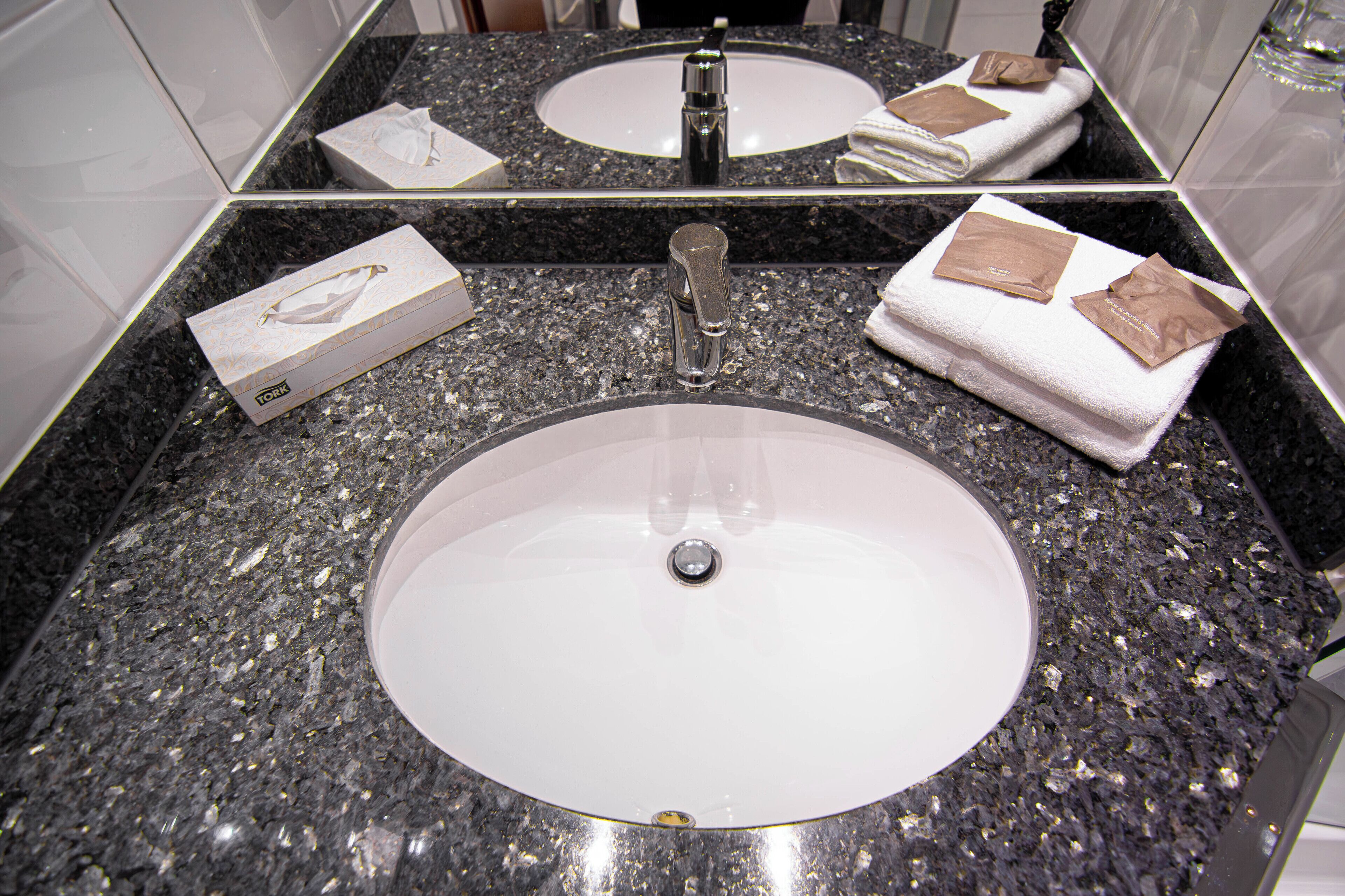 A bathroom with a granite countertop, two sinks, and a mirror.