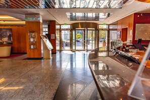 A modern hotel lobby with a revolving door, a reception desk, and a digital information kiosk.