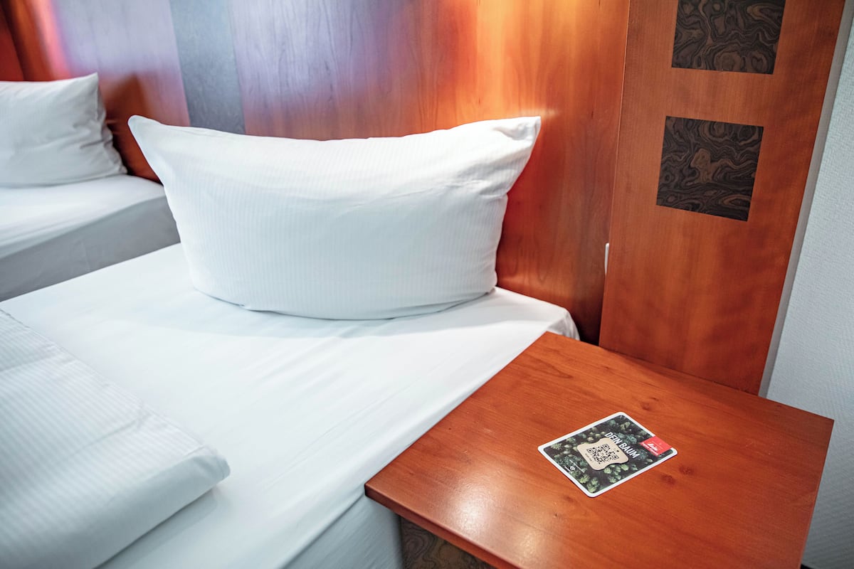 A hotel room with two beds, each with white bedding and pillows, a wooden nightstand with a card, and a wooden door with a patterned panel.
