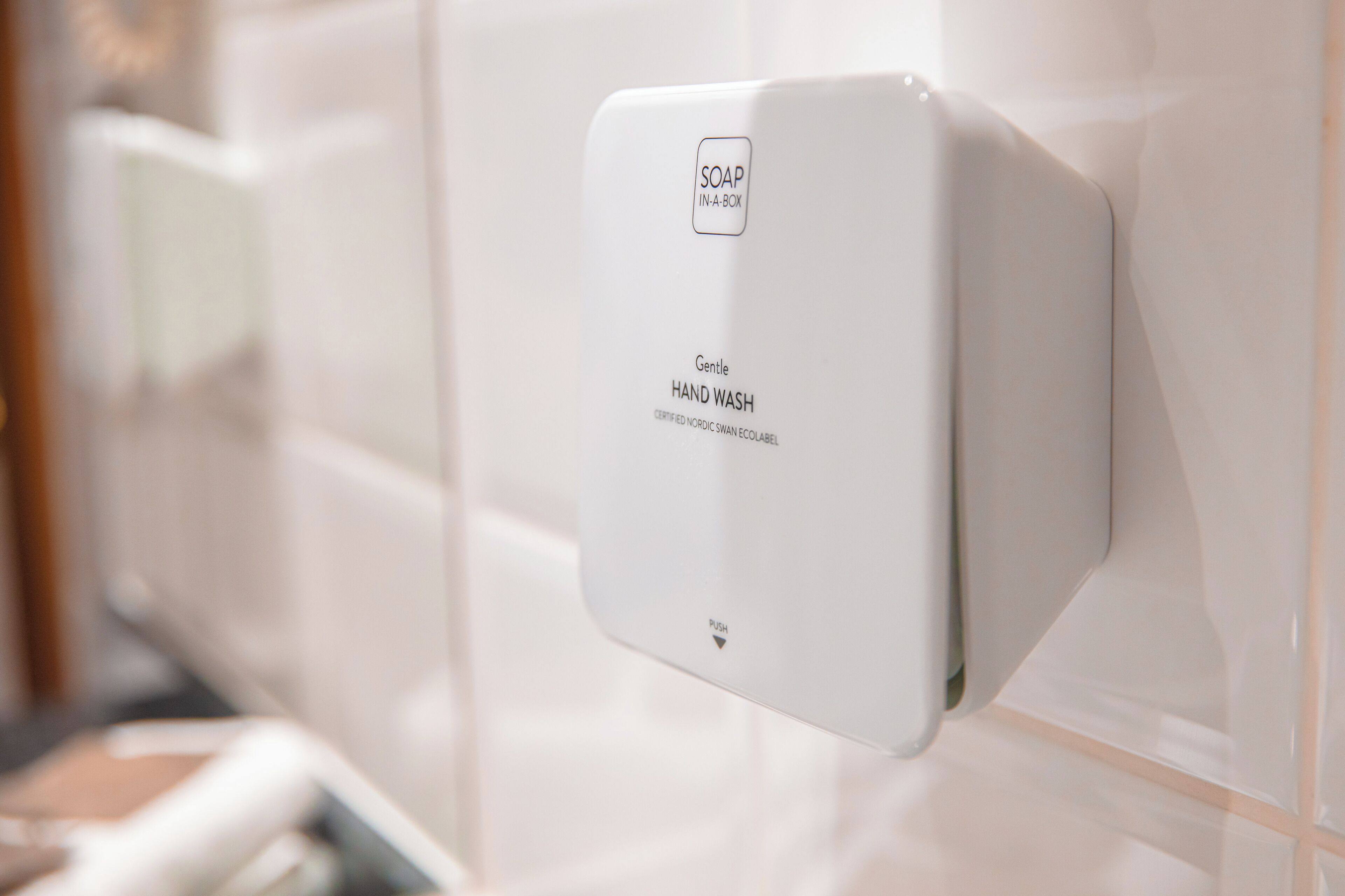 A wall-mounted soap dispenser with the label "Gentle HAND WASH" and "SOAP IN-A-BOX".