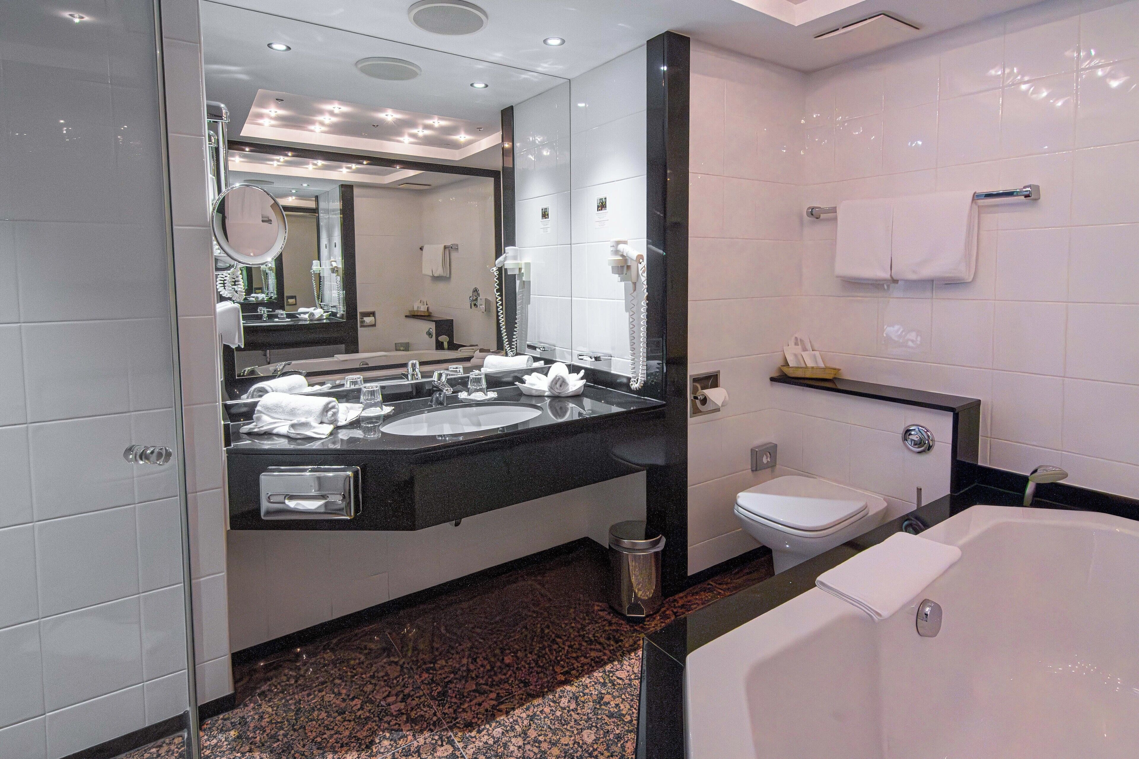 Et moderne badeværelse med dobbelt vask, toilet, badekar og et stort spejl.